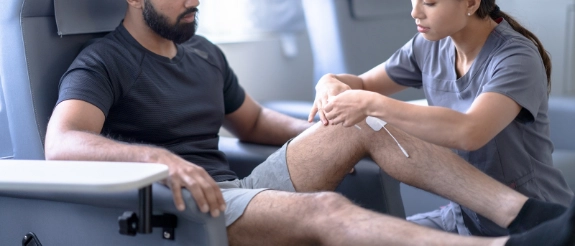 Physiotherapeutin behandelt Bein eines männlichen Patienten in einer Praxis.