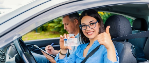 Frau mit Brille zeigt Daumen hoch im Auto neben Fahrer mit Führerschein