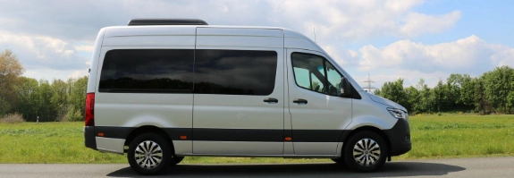 Weißer Wohnmobil-Kastenwagen steht auf Landstraße vor grüner Wiese und bewölktem Himmel