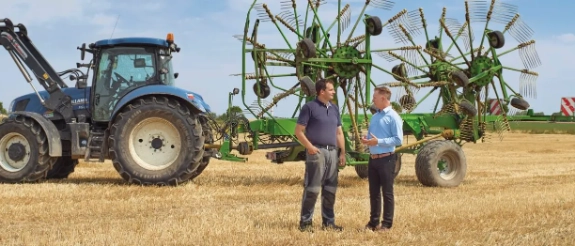 Zwei Männer in Geschäftskleidung besprechen sich vor grüner Landmaschine auf Feld