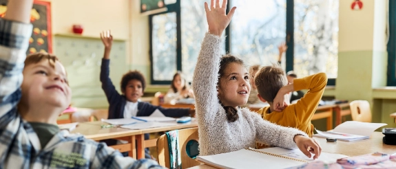 Schüler sitzen an ihren Tischen in der Schulklasse und melden sich eifrig im Unterricht.