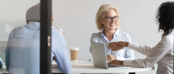Drei Geschäftsfrauen in einem Büro besprechen ein Projekt, eine sitzt am Laptop, die andere zeigt auf den Bildschirm.