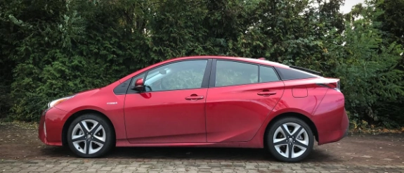 Roter Hybridwagen steht seitlich auf Pflastersteinen vor grüner Baumkulisse