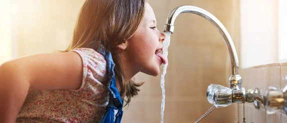 Mädchen trinkt Wasser direkt aus dem Wasserhahn im Badezimmer