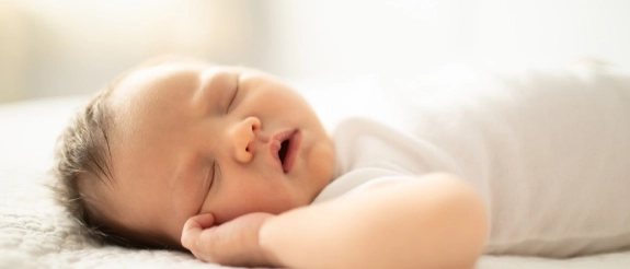 Neugeborenes Baby schläft friedlich auf weißem Bettlaken in heller, sonniger Umgebung
