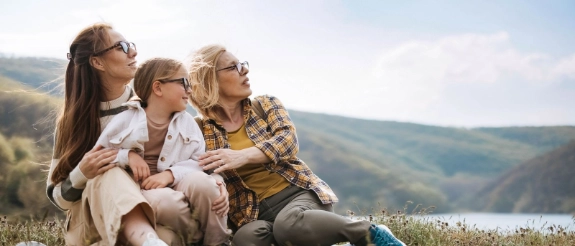 Drei Generationen sitzen zusammen in der Natur: Großmutter, Mutter und Tochter blicken zuversichtlich in die Zukunft..