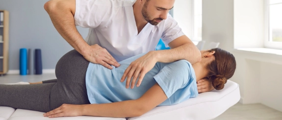 Physiotherapeut behandelt Patient auf Liege mit Bewegungsübung für Bein und Hüfte in Praxis