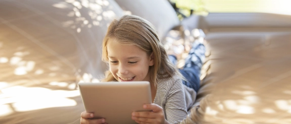 Lächelndes Mädchen hält Tablet in weihnachtlich dekoriertem Wohnzimmer mit Lichterketten