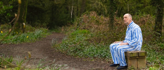 Verwirrter  alter Mann sitzt auf einer Bank im Wald in seinem Schlafanzug
