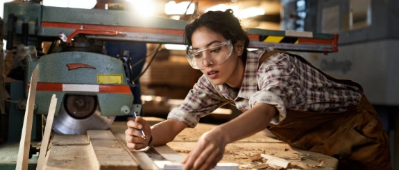 Eine junge Frau arbeitet vom Beruf her im Handwerk als Schreinerin und misst Holz aus.