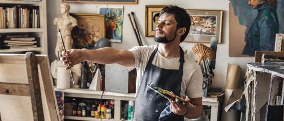 Ein junger Mann lächelt beim Malen, weil er frühzeitig für seine Altersvorsorge gesorgt hat.