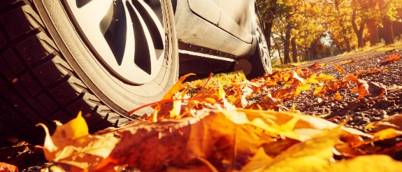 Auto mit Chromfelge auf herbstlichem Laubweg, Blätter in Orange und Rot