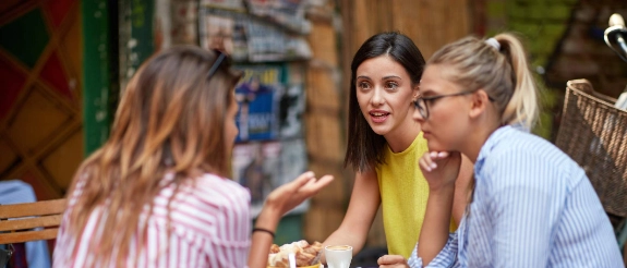 Drei junge Frauen sitzen im Cafe und diskutieren darüber, ob eine Berufsunfähigkeisversicherung sinnvoll ist.