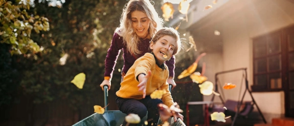 Mutter und Kind in gelber Jacke sammeln Kürbisse bei Herbstdeko im Garten bei Sonnenuntergang
