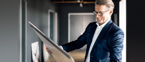 Geschäftsmann in dunklem Blazer und Brille betrachtet Baupläne in modernem Büro