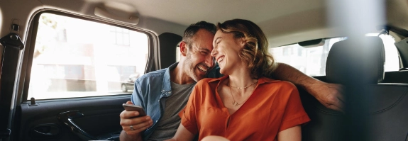 Mann und Frau lachen auf der Rückbank eines Autos.