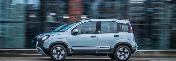 Silberner Fiat Panda fährt auf einer städtischen Straße, moderne Gebäude im Hintergrund, Bewegungsunschärfe