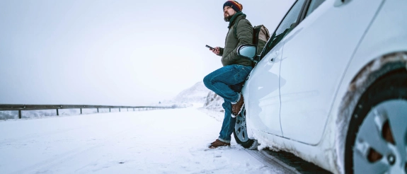 Mann lehnt sich an Auto im Winter.