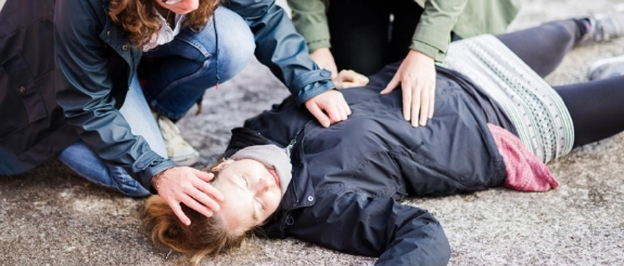 Frau liegt auf der Straße, während eine andere Person sie unterstützt und beruhigt nach einem Unfall oder medizinischen Notfall.