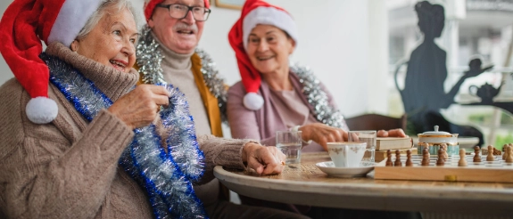Mehrere alte Personen haben eine Weihnachtsmütze auf und sitzen gemeinsam an einem Tisch und trinken dort Tee.