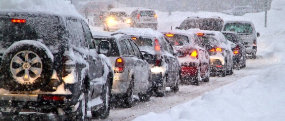 Mehrere Autos stehen im dichten Schneefall hintereinander auf einer verschneiten Straße im Stau.