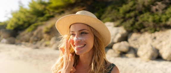 Frau mit Strohhut und Sonnenbrille am Strand, Wald im Hintergrund, sonniger Tag