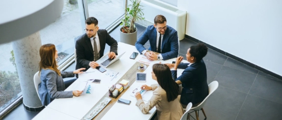Vier Geschäftspersonen sitzen an einem Tisch in einem modernen Büro und diskutieren über Dokumente und Tablets.