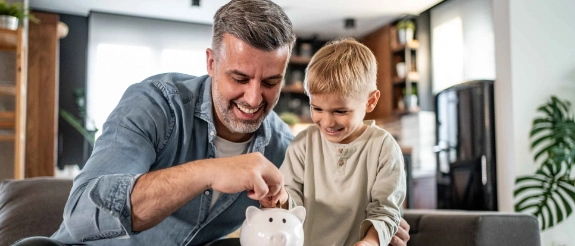 Ein Junge legt Münzen in ein Glas als Symbol für das Kindergeld, dass seine Eltern für ihn anlegen konnten. 
