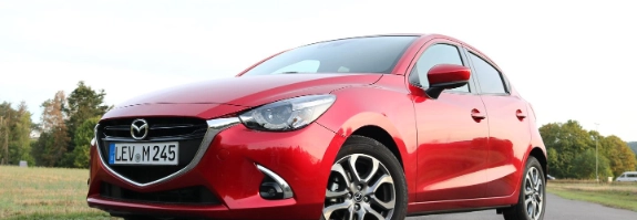 Roter Mazda2 Kleinwagen auf Parkplatz, Seitenansicht mit Blick auf Frontdesign und Räder