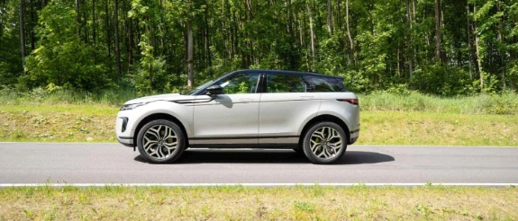 Silberner Cabrio-SUV auf Landstraße mit Wald im Hintergrund und grüner Wiese