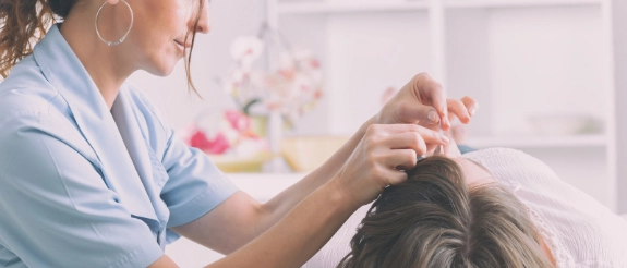 Friseurin schneidet Haare einer Kundin im hellen Salon mit rosafarbener Dekoration im Hintergrund