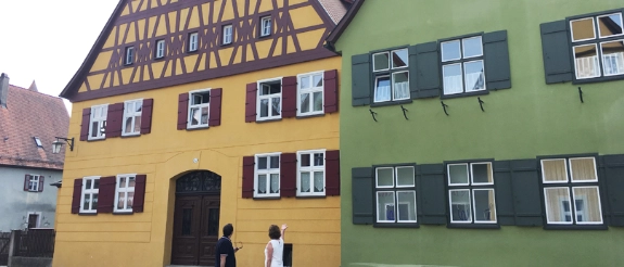Fachwerkhäuser und grünes Gebäude in malerischer Altstadt, zwei Personen stehen auf gepflastertem Platz