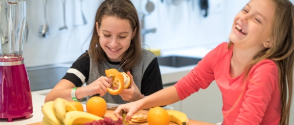 Zwei Mädchen in einer Küche sortieren frisches Obst und Gemüse auf einem Tisch.