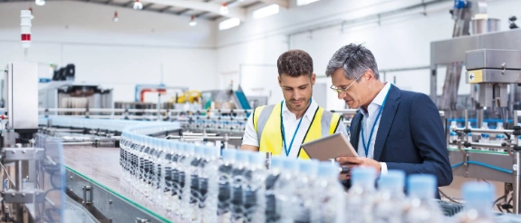 Zwei Mitarbeiter mit Warnwesten prüfen Wasserflaschen in einer modernen Produktionshalle