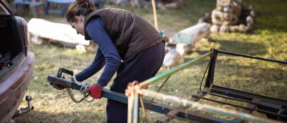 Person in blauer Kleidung arbeitet an Holzkonstruktion im Garten, umgeben von Bäumen und Gartengeräten