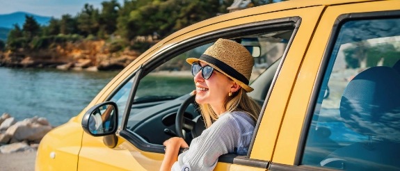 Eine Frau mit einer Sonnenbrille sitzt im Auto und schaut aus dem Fenster in Richtung Meer . 