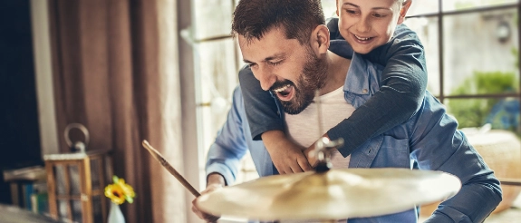 Vater und Sohn backen zusammen in der Küche, Kind sitzt auf Schultern des Mannes, beide lächeln glücklich.