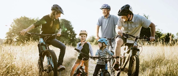 Familie mit Kindern fährt Fahrrad in ländlicher Umgebung, Eltern und Kinder auf Rädern in Wiese mit Bäumen