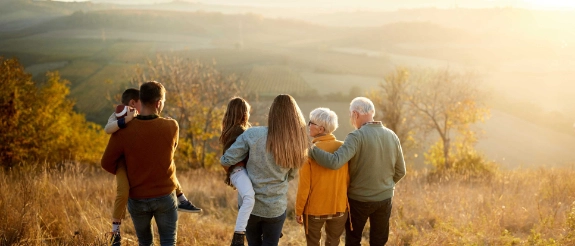 Mehrgenerationenfamilie steht auf Hügel mit Herbstwald und Nebeltal im Hintergrund