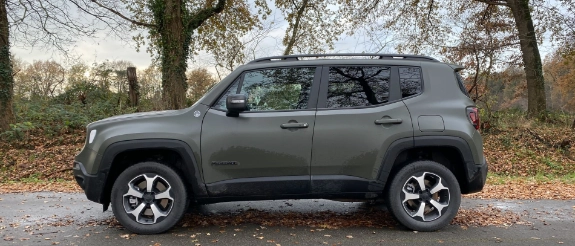 Grauer SUV Jeep Renegade im Profil auf herbstlicher Straße mit Laubbäumen im Hintergrund