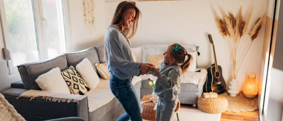 Mutter und Tochter springen gemeinsam im Wohnzimmer.