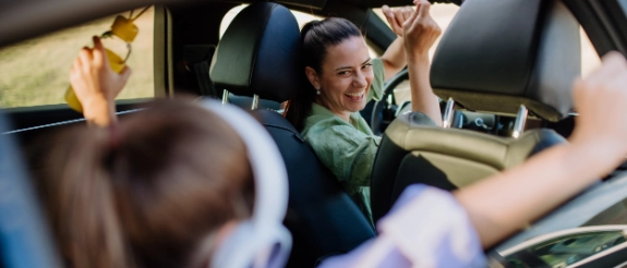 Frau im Auto hebt Arm triumphierend, während Passagiere applaudieren und jubeln beim Sieg.