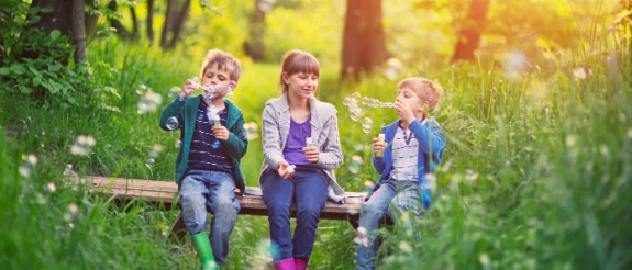 Kinder machen Seifenblasen in der Natur und fühlen sich sicher, weil ihre Eltern an die Kinderabsicherung gedacht haben.