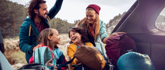 Glückliche Familie packt den Kofferraum ihres Autos.