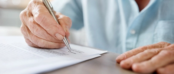 Eine ältere Person unterschreibt mit einem Stift auf einem Dokument