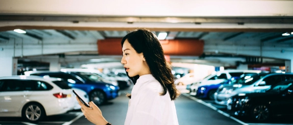Junge Frau steht in einer Tiefgarage und schaut auf ihr Handy.