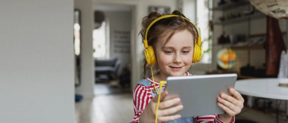 Lächelndes Kind mit gelben Kopfhörern hält Tablet in der Hand und schaut auf den Bildschirm.