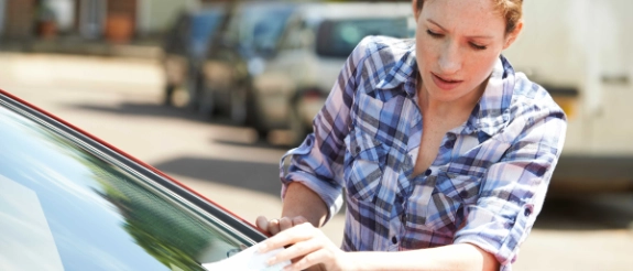 Eine Frau entfernt einen Strafzettel von der Windschutzscheibe ihres Autos.