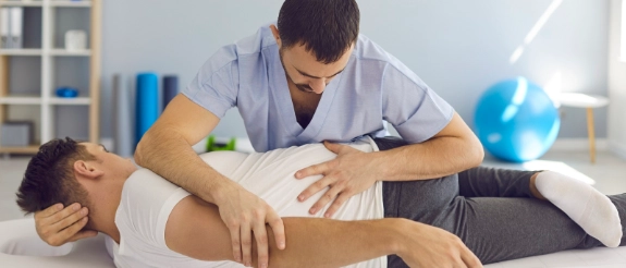 Physiotherapeut untersucht Arm einer Patientin auf Behandlungsliege in heller Praxis