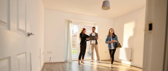 Immobilienmakler zeigt jungem Paar moderne Wohnung mit hellem Flur und Holzboden